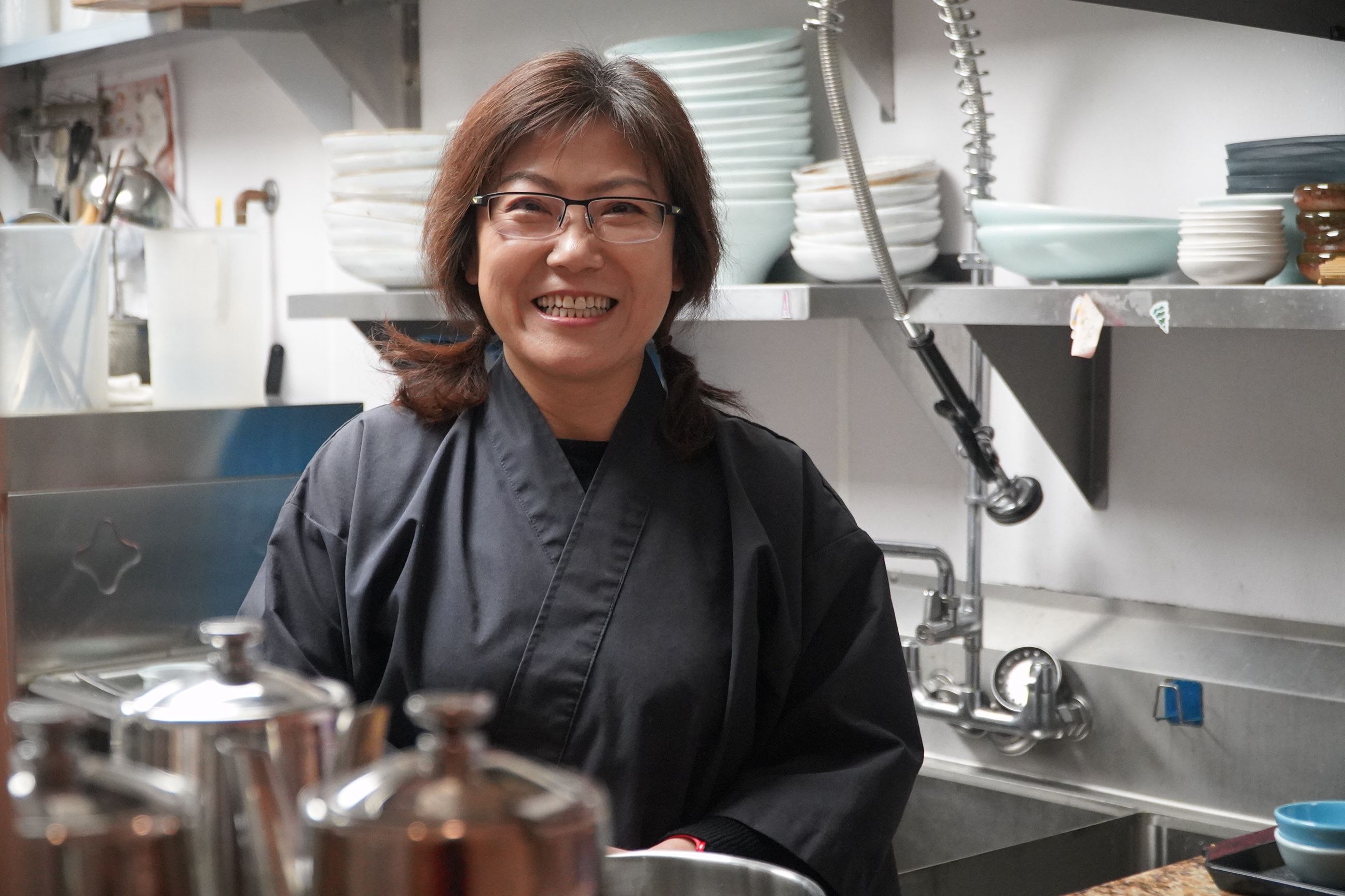 Li Ma is standing in the kitchen of her Japanese restaurant, smiling at the camera.